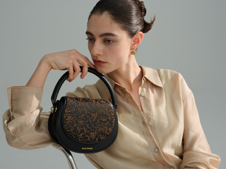 Embroidered black leather handbag, elegant female model side profile shot holding the top handle bag