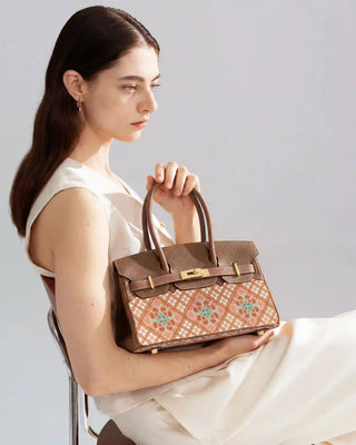 Brown caisson-pattern brocade & leather handbag with gold hardware, side half-body view of female model in white outfit