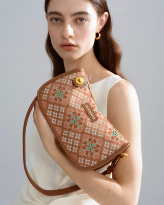 Front half-body view of female model in white outfit holding a brown caisson-pattern brocade shoulder bag with gold hardware