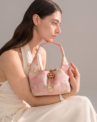 Pink floral brocade hobo handbag with delicate pattern and gold hardware, side half-body view of female model in white outfit