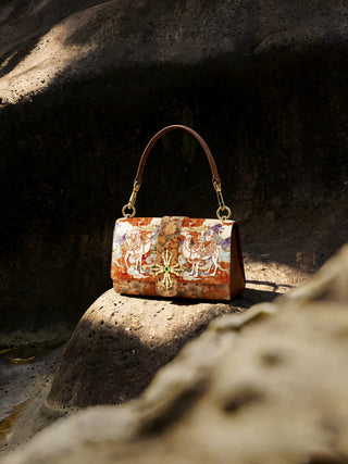 A brown embroidered leather bag placed on a rock in direct sunlight