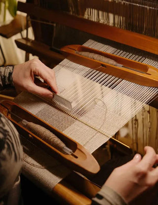 Artisan hands weaving natural silk fabric on a traditional wooden loom, showcasing Silkyhaus's meticulous handcrafted textile process for luxury accessories