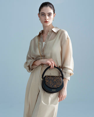 Front half-body view of model carrying the silkyhaus black embroidered leather handbag with gold hardware