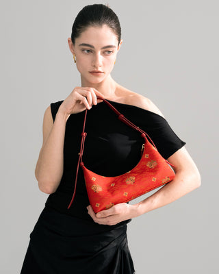 Front half-body view of female model carrying the silkyhaus brocade leather hobo handbag with gold hardware