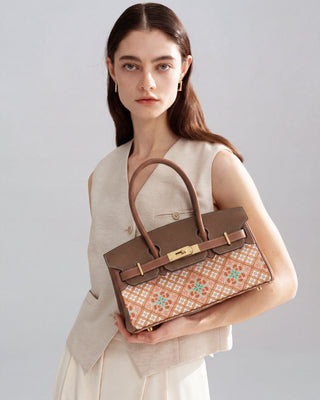 Front half-body view of model holding Silkyhaus brown top-handle handbag with caisson ceiling pattern and gold hardware.